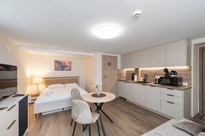 Ein modernes Hotelzimmer mit Bett, Nachttisch, Lampe, Sessel, rundem Tisch und Küchenzeile.