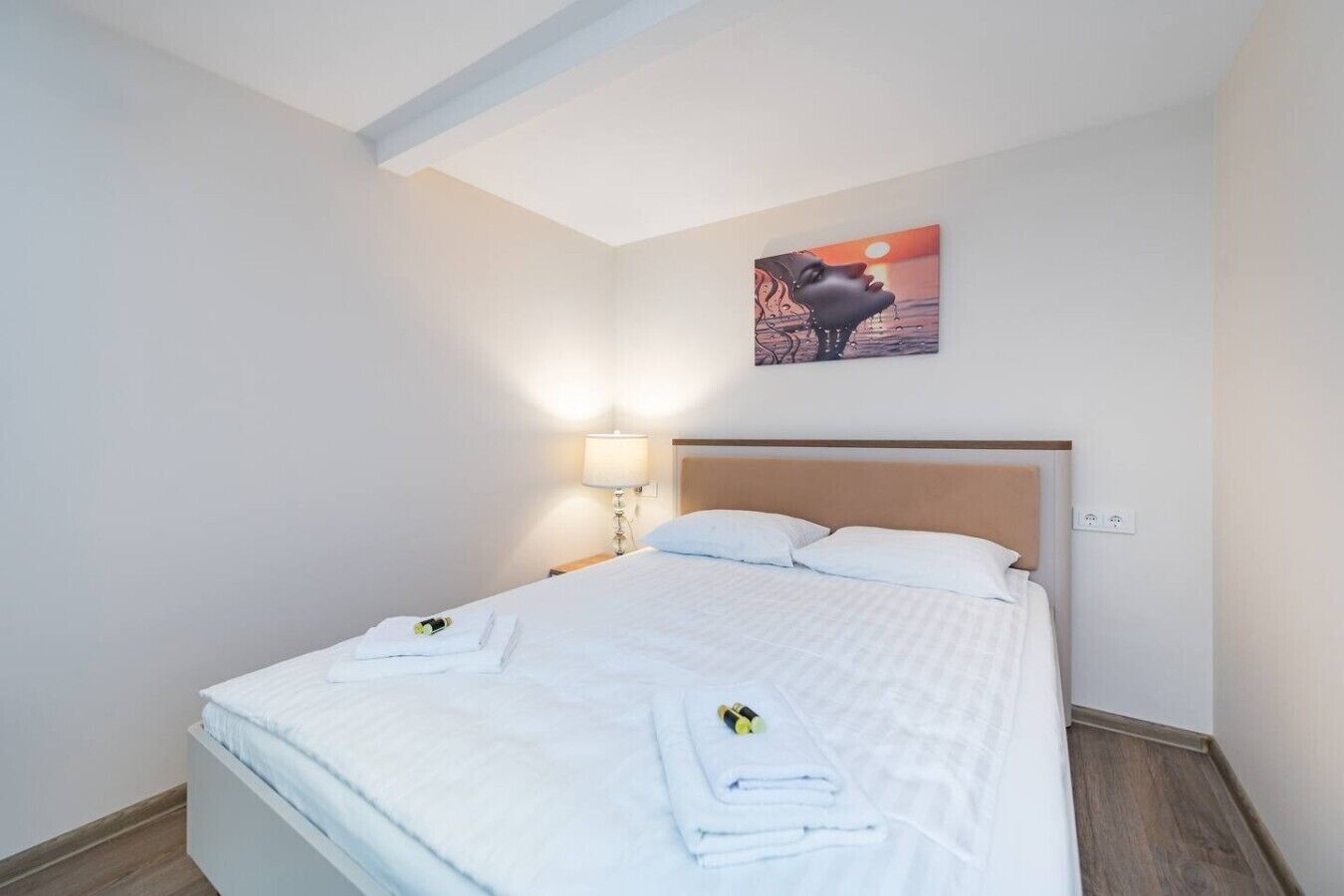 Een keurig opgemaakt bed met witte lakens, een hoofdbord en een aan de muur hangend schilderij.