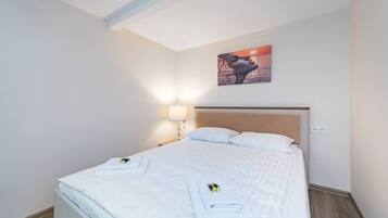 Een keurig opgemaakt bed met witte lakens, een hoofdbord en een aan de muur hangend schilderij.