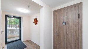 Un couloir avec une porte en bois portant l’inscription « 101 », une porte noire avec une poignée en métal, une horloge murale en bois et une petite caméra de surveillance.