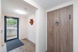 Ein Flur mit einer Holztür mit der Aufschrift '101', einer schwarzen Tür mit einem Metallgriff, einer Holz-Wanduhren und einer kleinen Überwachungskamera.