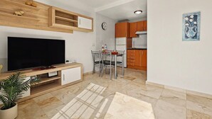 A modern living room with a flat-screen TV, a dining area with a table and chairs, and a kitchen with wooden cabinets and a refrigerator. - Vacation Apartment 'Olga' with Shared Pool, Private Terrace and Wi-Fi (Castillo Caleta de Fuste)