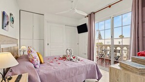 A hotel room with a bed, a TV, a balcony with a table and chairs, and a view of the outside. - Vacation Apartment 'Olga' with Shared Pool, Private Terrace and Wi-Fi (Castillo Caleta de Fuste)