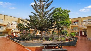A courtyard with a large tree, potted plants, a wooden bench, and a tiled floor. - Vacation Apartment 'Olga' with Shared Pool, Private Terrace and Wi-Fi (Castillo Caleta de Fuste)