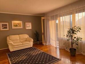 Una sala de estar con un sofá, un tapete estampado, una planta en maceta y cuadros en la pared.