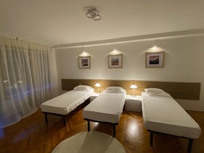 Una camera d'albergo con tre letti singoli, una testiera in legno, un tavolino e tre quadri appesi alle pareti.