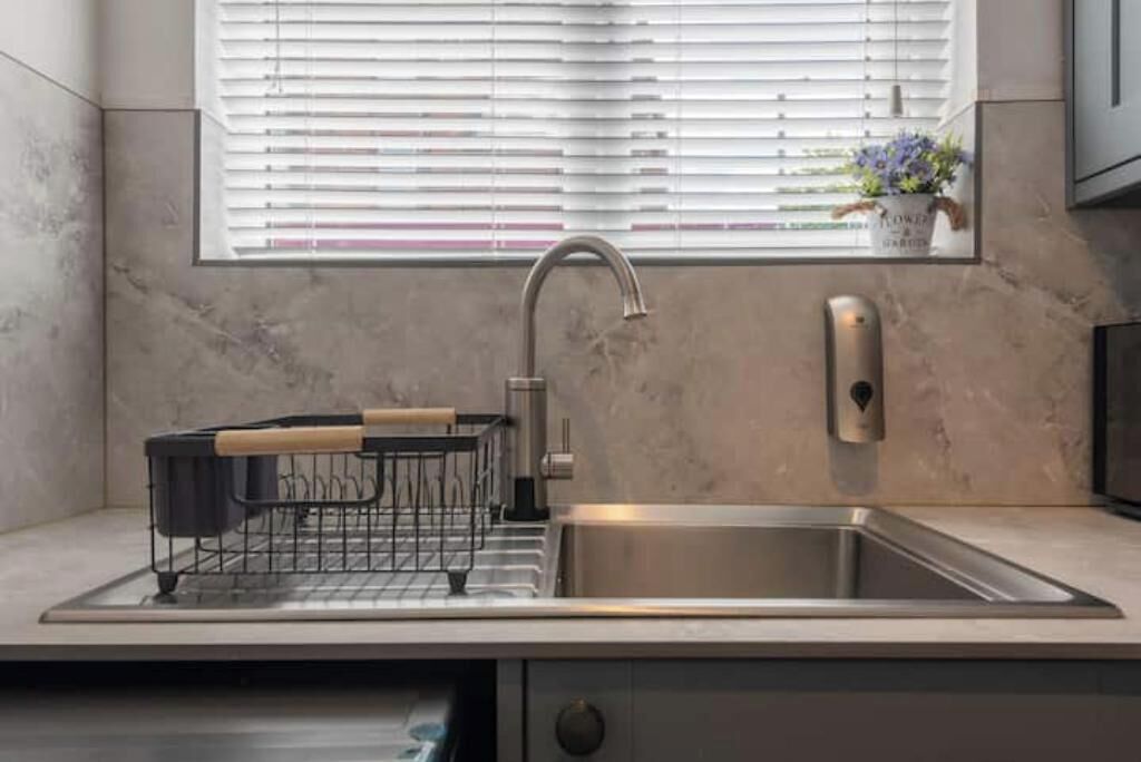 A modern kitchen with a stainless steel sink, a dish rack, and a window with blinds.