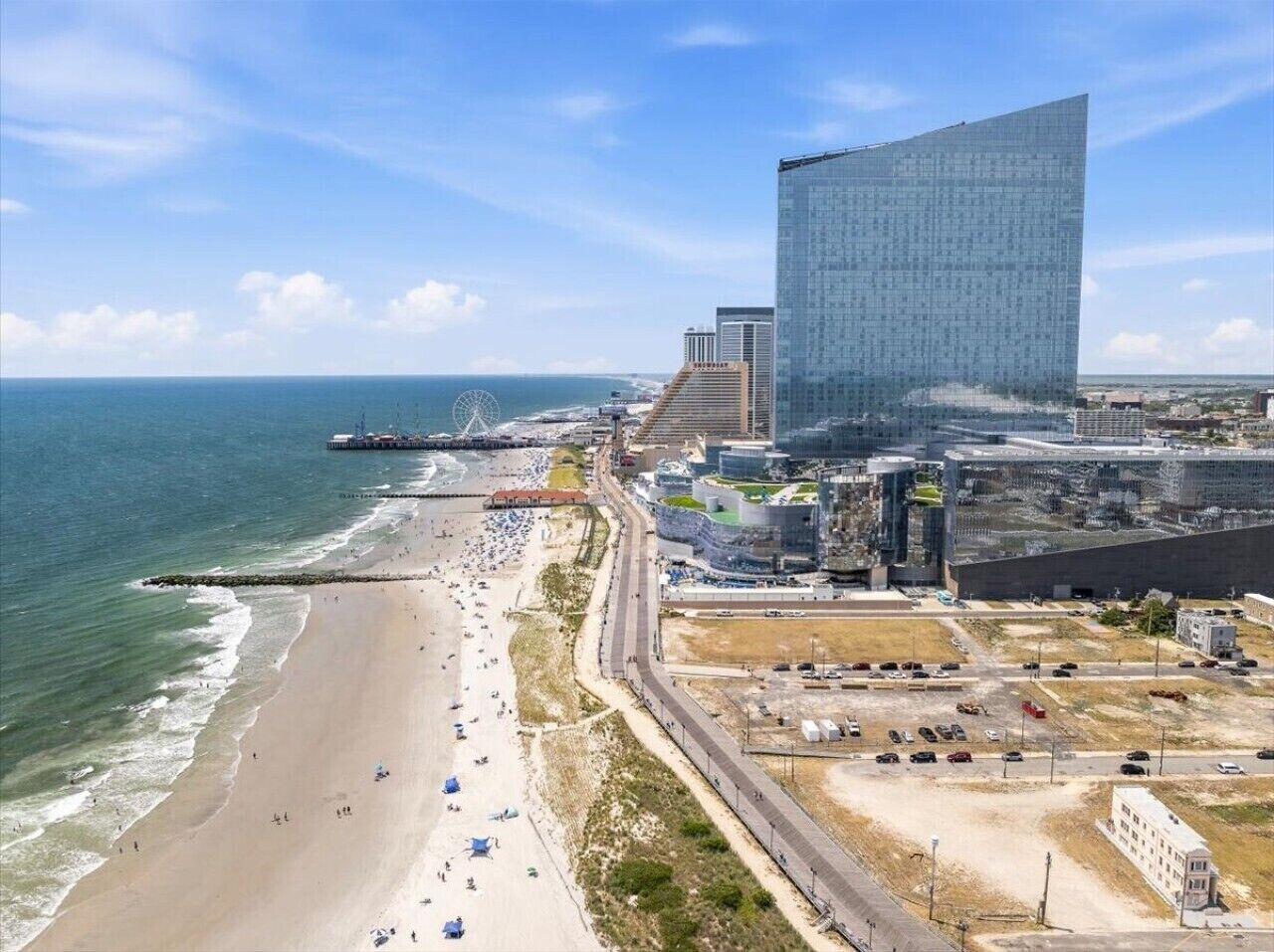A coastal cityscape with a beach, a large modern building, and a Ferris wheel in the distance.