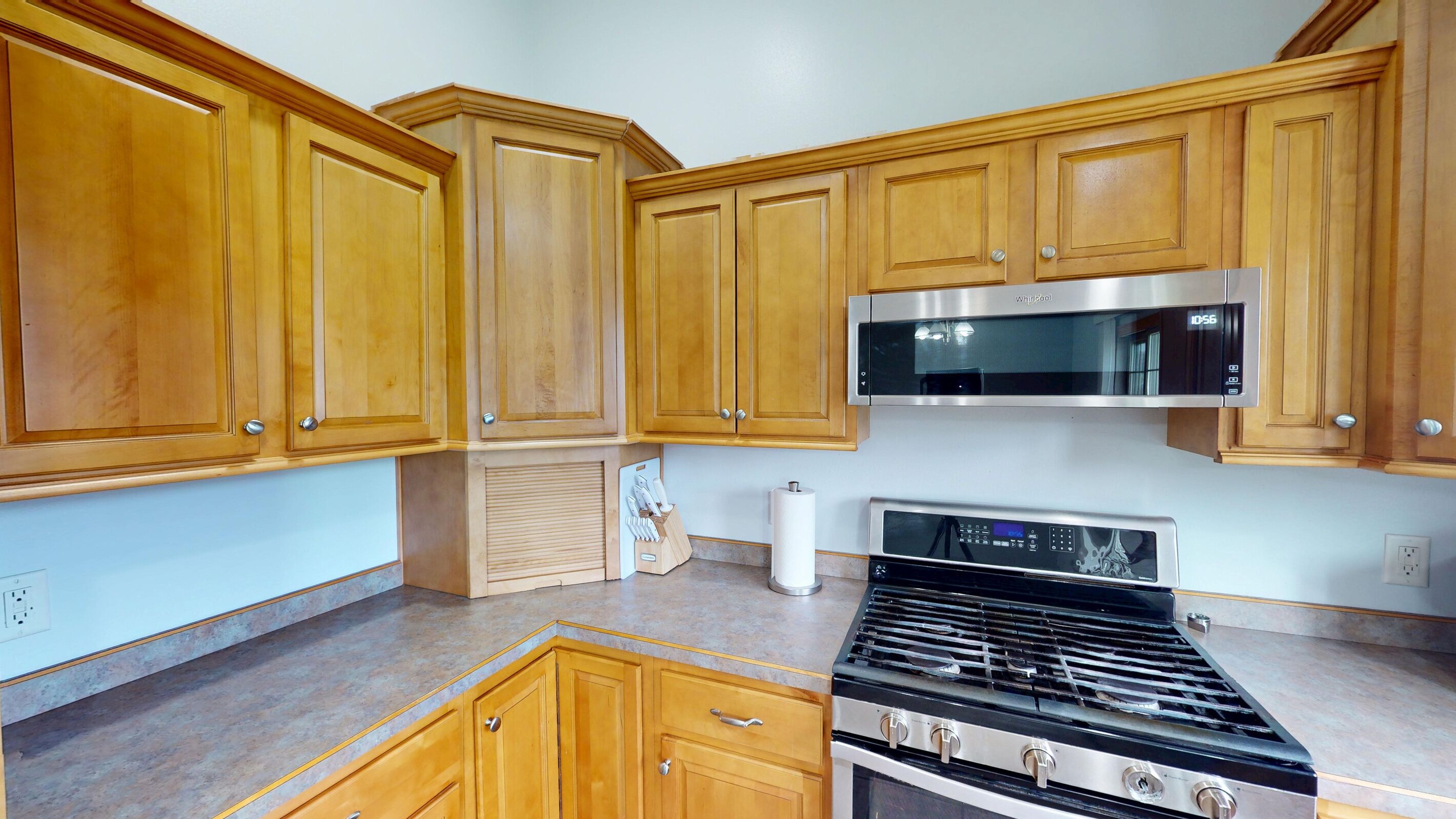 Una cocina con armarios de madera, un microondas de acero inoxidable y una estufa a gas.