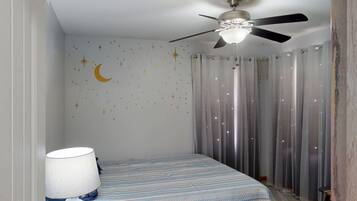 A bedroom with a bed, a ceiling fan, a night lamp, and curtains.