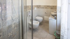 Ein Badezimmer mit Dusche, zwei Toiletten, einem Waschbecken und einem Mülleimer.