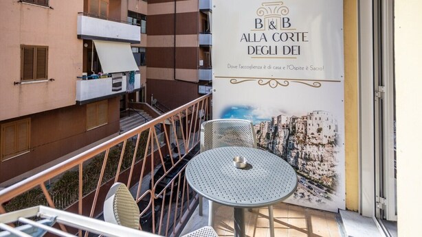 Ein Balkon mit Tisch, Stühlen und Geländer, sowie ein Schild für 'B&B Alla Corte Degli Dei' und Blick auf die Stadt.