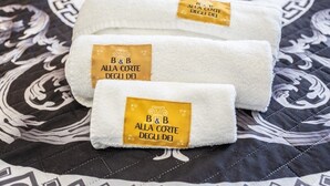 Three folded towels with a label on a patterned bedspread. - At the Court of the Gods - Estia Room (Tropea)