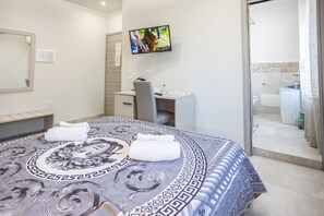A hotel room with a bed, a desk, a chair, a television, and a bathroom visible through an open door.