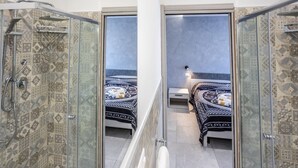 A mirrored room with a shower, a bed with patterned bedding, and a nightstand. - At the Court of the Gods - Estia Room (Tropea)