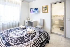 A hotel room with a bed, a desk, a chair, a TV, and a bathroom visible through an open door.