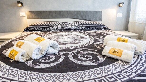 A bed with a patterned bedspread, a headboard, and three towels with labels. - At the Court of the Gods - Aphrodite Room (Tropea)