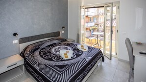 A modern bedroom with a large bed, a desk, and a balcony with outdoor seating. - At the Court of the Gods - Aphrodite Room (Tropea)