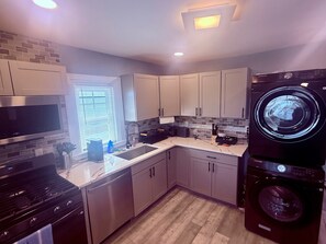 A modern kitchen with a built-in washer and dryer, stainless steel appliances, and a window with blinds. - New! Ocean Pearl - 2nd Home from Beach + Boardwalk (Seaside Park)
