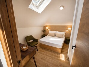 Ein Schlafzimmer mit Dachfenster, einem Bett, einem Sessel, einem Nachttisch und einer kleinen Pflanze.
