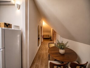 Ein schmaler Flur mit Holzboden, einem Esstisch mit Stühlen, einem Kühlschrank und einem Spiegel.