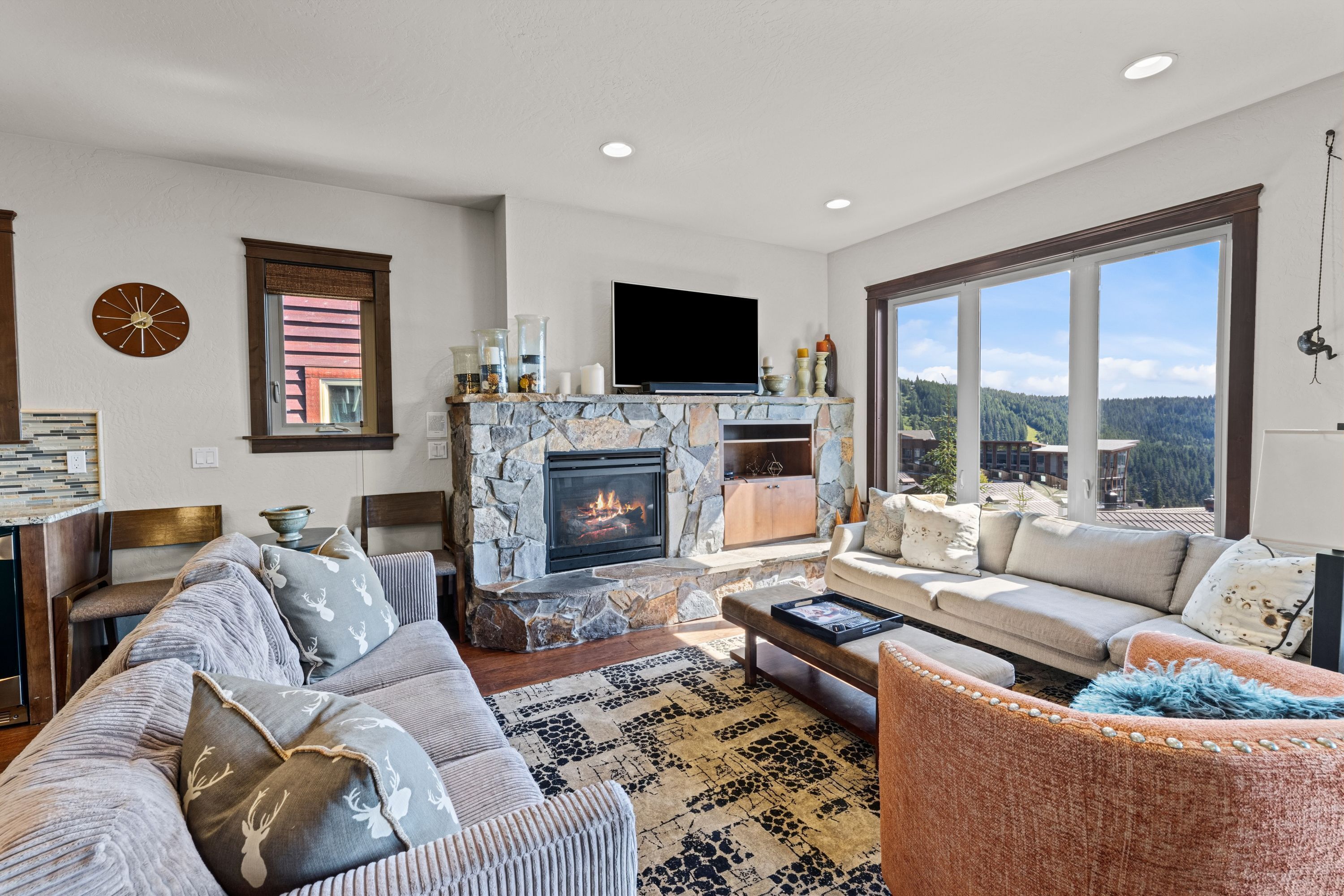 A living room with a stone fireplace, a large window, a television, and a sofa.