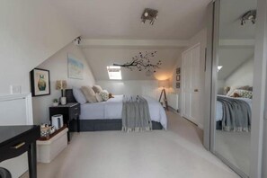Ein Schlafzimmer mit einem Bett, Nachttischen, einem Schreibtisch, einem Spiegel und einem Fenster.