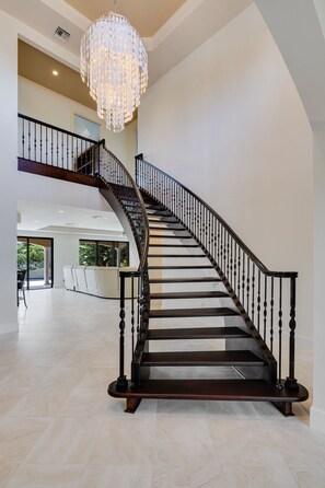 A grand staircase with a chandelier, leading to a second floor with a balcony.