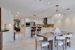 Une cuisine moderne avec des meubles blancs, un îlot central doté de tabourets de bar et un luminaire suspendu.