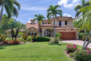 A Mediterranean-style house with a red-tiled roof, arched windows, and a well-maintained garden with palm trees and flowering plants.
