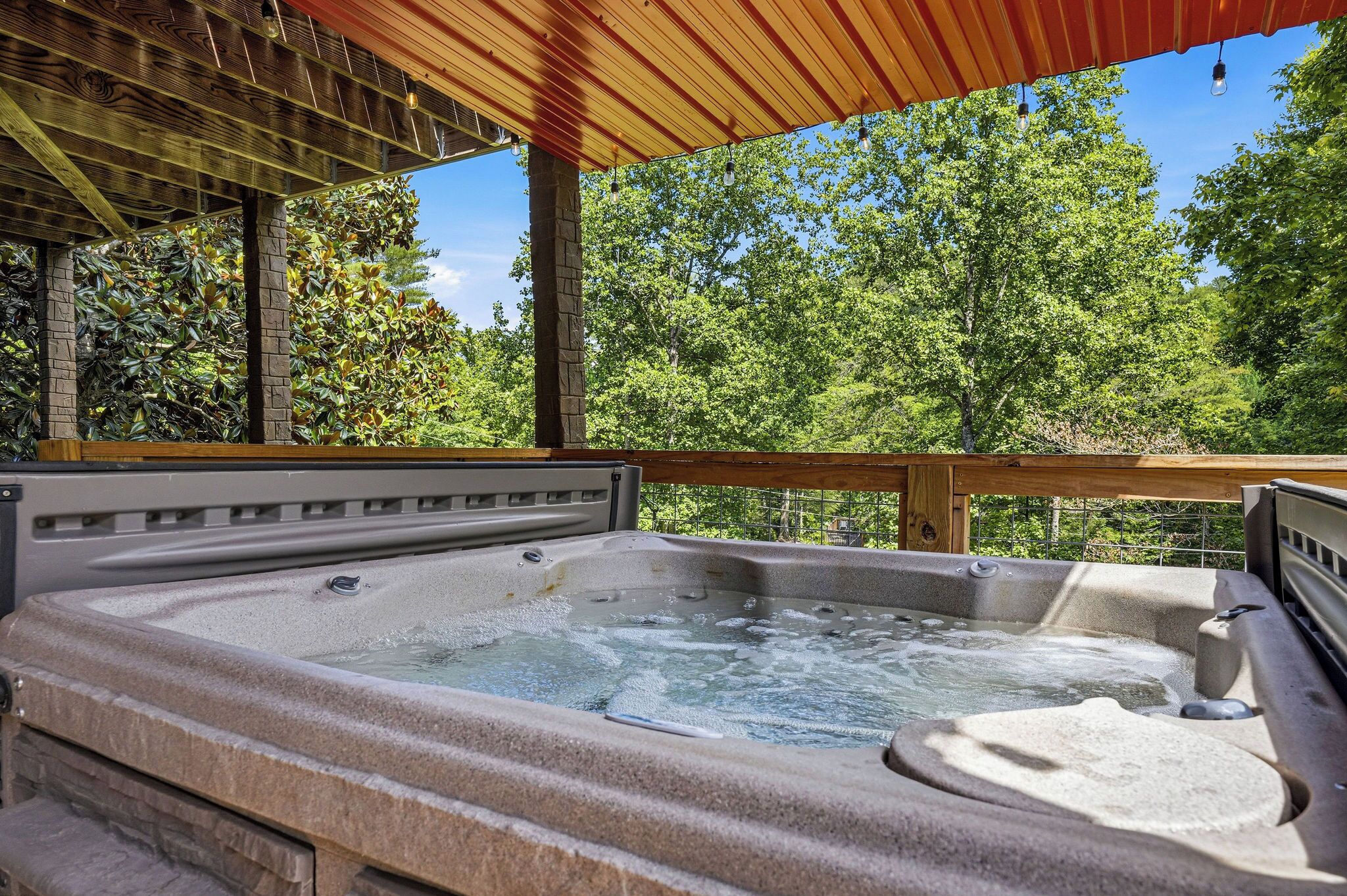 Een hottub onder een houten pergola, met uitzicht op bomen.