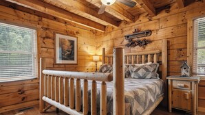 Un dormitorio de cabaña de madera con cama, mesita de noche, ventana y ventilador de techo.