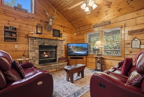 A log cabin interior with a stone fireplace, leather sofas, a television, and a window with blinds. - Relax and have Adventure Here! (PIGEON FORGE)