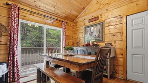 Interior de una cabaña de madera con una mesa de comedor, un banco y un cuadro en la pared.