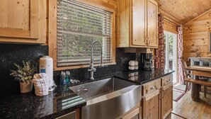 Cocina de cabaña de madera con un ventanal grande, pileta de acero inoxidable y gabinetes de madera.