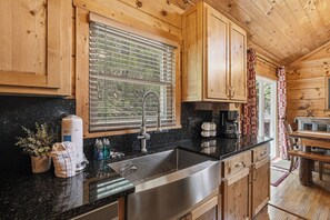 A wooden cabin kitchen with a large window, stainless steel sink, and wooden cabinets. - Relax and have Adventure Here! (PIGEON FORGE)