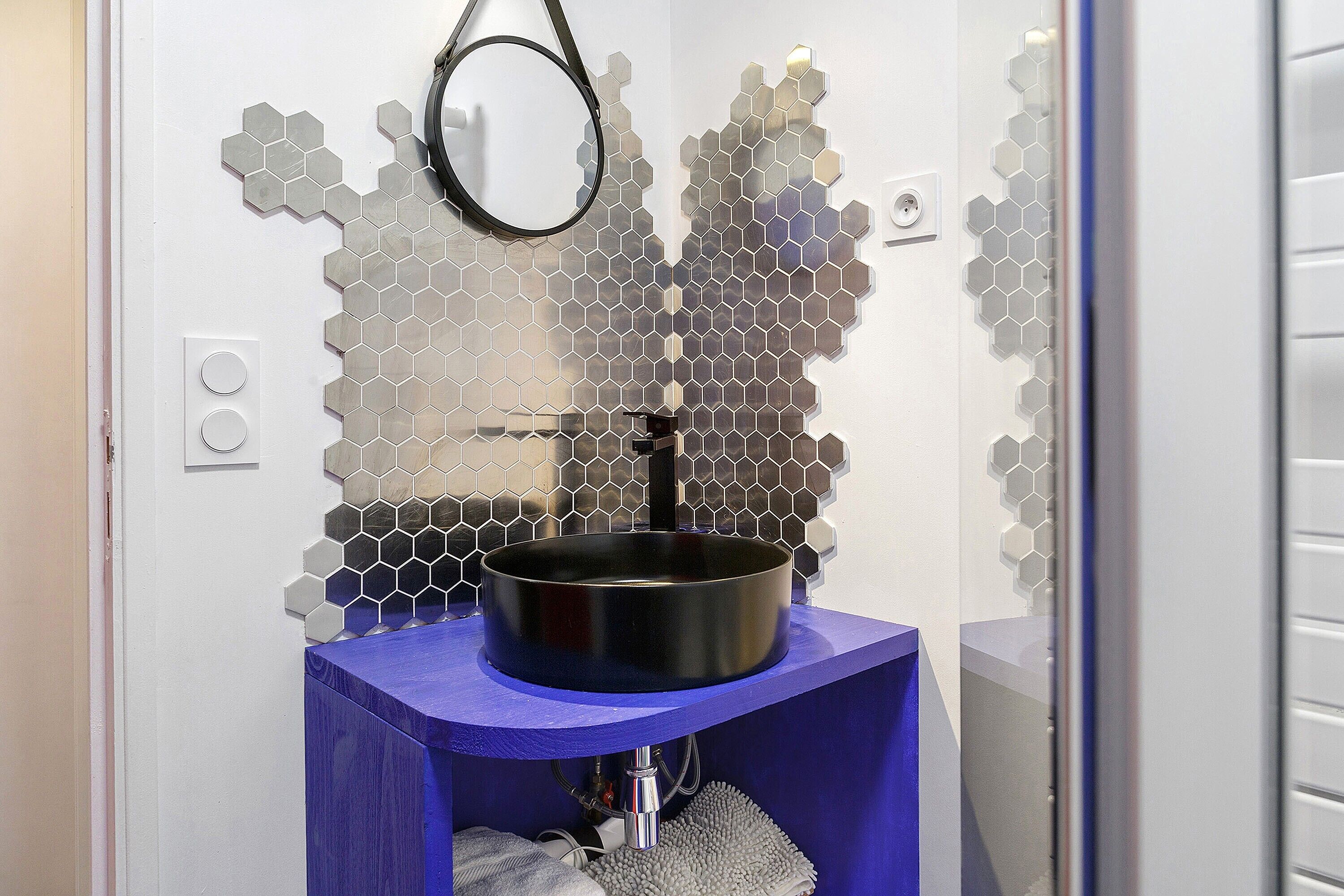Un baño con un lavamanos moderno, un espejo y un original salpicadero de azulejos hexagonales.