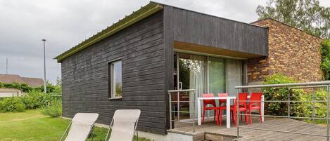 A modern house with a deck, two lounge chairs, and a table with red chairs.