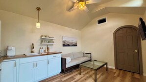 A compact living space with a kitchenette, a sofa, a glass coffee table, a ceiling fan, and a door. - Petite Palace: Guest home in Louisburg, NC (Louisburg)
