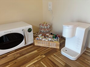 Un microondas, una cafetera y un soporte para cápsulas de café sobre un piso de madera.