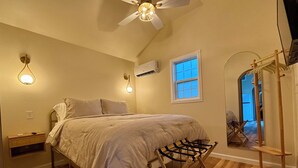 A bedroom with a bed, a ceiling fan, an air conditioner, a window, and a wooden rack. - Petite Palace: Guest home in Louisburg, NC (Louisburg)