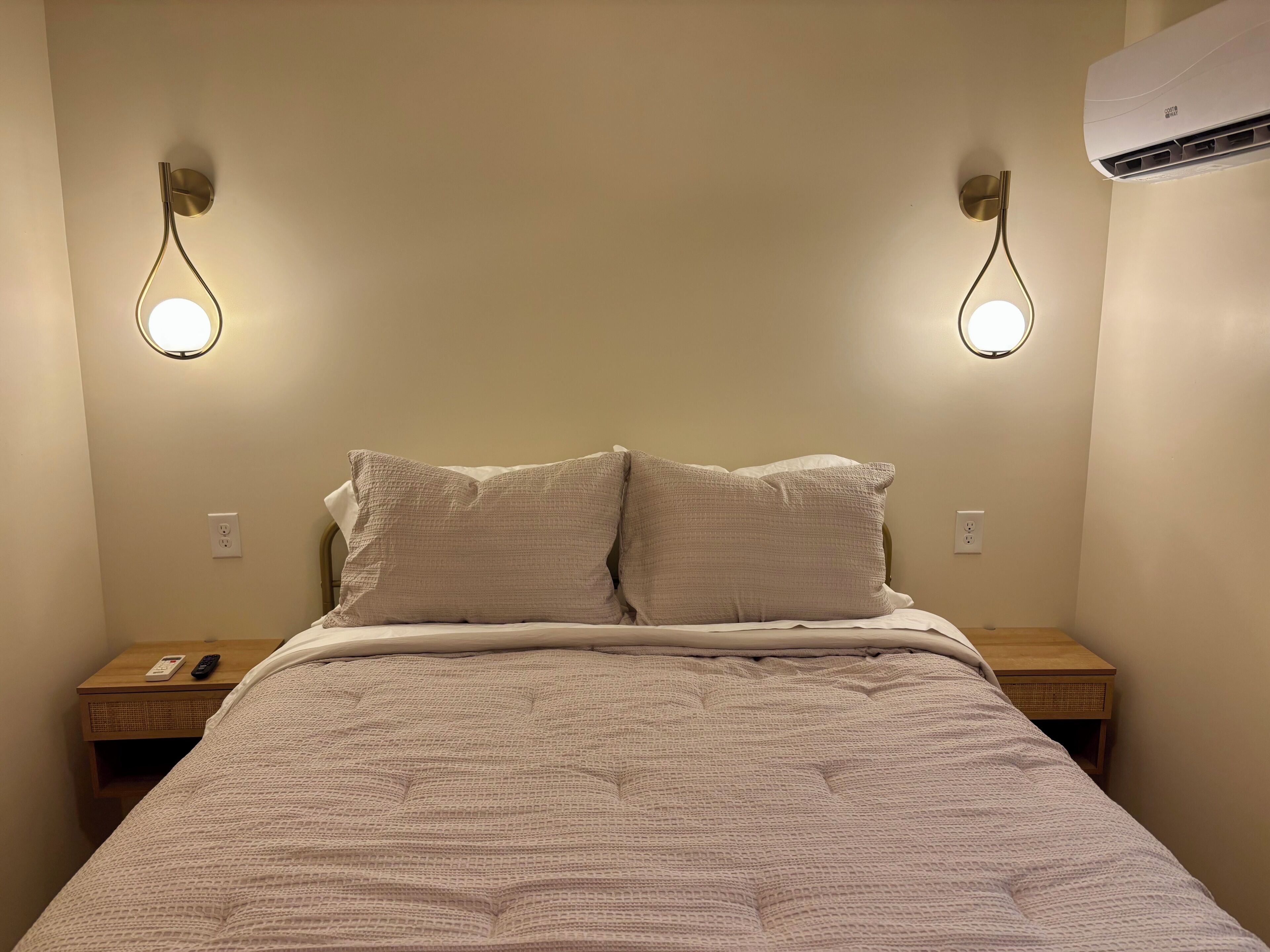 A bed with a textured blanket, two bedside tables with lamps, and an air conditioner on the wall.