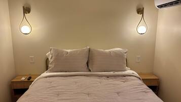 A bed with a textured blanket, two bedside tables with lamps, and an air conditioner on the wall.