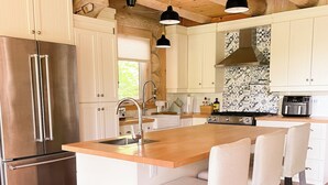 Une cuisine avec des poutres en bois, un réfrigérateur en acier inoxydable, un grand îlot central avec des tabourets de bar et un crédence décorée.