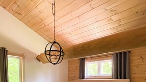 Une chambre avec un plafond en bois, un lit avec une literie blanche, deux tables de chevet avec des lampes et une fenêtre avec des rideaux.