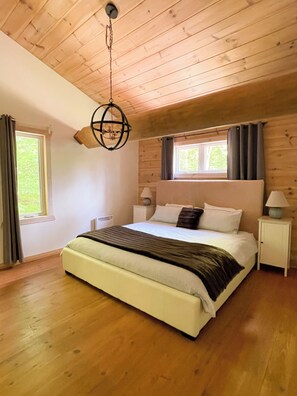 A bedroom with a wooden ceiling, a bed with white bedding, two bedside tables with lamps, and a window with curtains. - Premium log cabin, peaceful cozy retreat in nature, nearby Golf Montebello (Montebello)