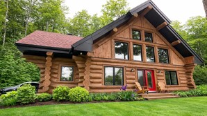 Une cabane en rondins avec une porte rouge, de grandes fenêtres et un toit en pente.