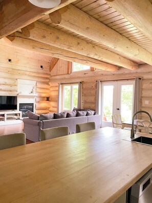 A log cabin interior with a dining area, sofa, television, and kitchen.