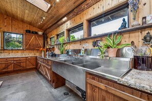 Eine Küche mit Holzausstattung, einem großen Edelstahlspülbecken und einem Fenster mit Blick auf Grünflächen.