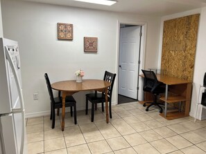 Ein Essbereich mit einem runden Tisch, vier Stühlen, einer Blumenvase, zwei gerahmten Bildern an der Wand, einer Tür und einem Holztisch mit einem Stuhl.